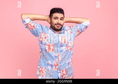 Ritratto di un uomo rilassato e bello in camicia blu casual, in piedi con mano dietro la testa e sorridente, guardando la macchina fotografica. Monolocale interno Foto Stock