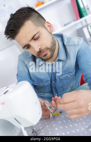 giovane uomo allegro sarto che lavora sulla macchina da cucire Foto Stock