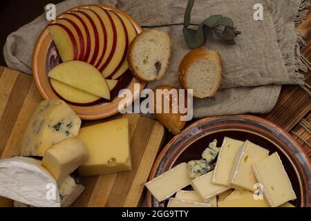 Diversi tipi di formaggio con mela affettata su un piano di taglio rustico in legno. Vista dall'alto Foto Stock