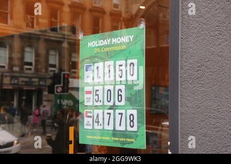 Glasgow, Scozia, ago 2021. Bella bionda giovane caucasica donna controllare i tassi di valuta su un poster temporaneo Foto Stock