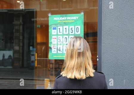 Glasgow, Scozia, ago 2021. Bella bionda giovane caucasica donna controllare i tassi di valuta su un poster temporaneo Foto Stock