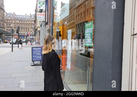 Glasgow, Scozia, ago 2021. Bella bionda giovane caucasica donna controllare i tassi di valuta su un poster temporaneo Foto Stock