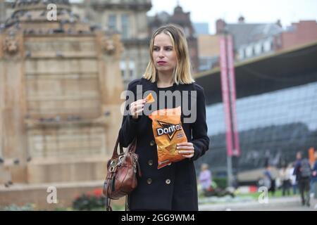 Glasgow, Scozia, ago 2021. Bella bionda giovane donna caucasica che mangia un pacchetto di Doritos in George Square, Glasgow. Foto Stock