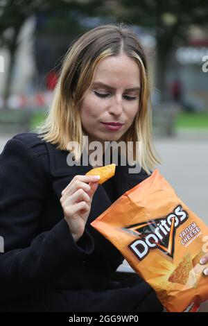 Glasgow, Scozia, ago 2021. Bella bionda giovane donna caucasica che mangia un pacchetto di Doritos in George Square, Glasgow. Foto Stock