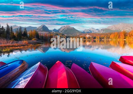 Pittoresca vista autunnale del lago Strbske pleso nel Parco Nazionale di High Tatra, Slovacchia. Fila di barche di legno rosso e alte montagne sullo sfondo. Fotografia di paesaggio Foto Stock