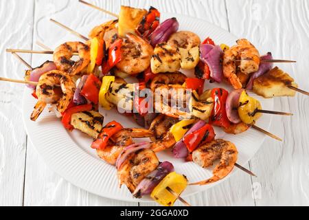 Gamberi Kabobs alla griglia con cipolla rossa, pepe dolce e ananas su un piatto bianco, primo piano Foto Stock