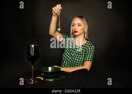 Bella giovane donna strega con rossetto rosso sulle labbra e conjure trucco su sfondo nero, rituale magico per la ricchezza. Foto Stock