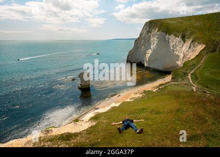 Uomo che posa in erba. Bat's Head scogliere, a ovest di Durdle Door. Lulworth Estate, Dorset, Regno Unito. Ago 2021 Foto Stock