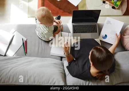 Direttamente sopra la vista della madre incinta seduta con il laptop sulle ginocchia e lavorare con le finanze mentre suo figlio parla con lei Foto Stock