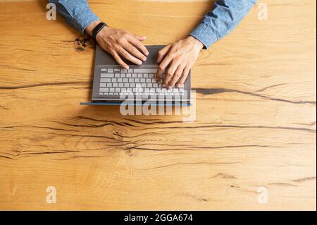Vista dall'alto a mani di businessman stanno digitando e usando la tastiera del laptop, ricercando, navigazione di fotoricettore, trasmettendo e rispondendo alle email, sulla scrivania di legno Foto Stock
