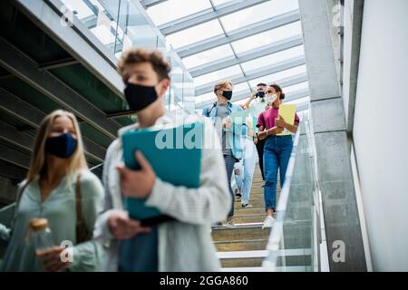 Studenti universitari che camminano lungo le scale e parlano al chiuso, concetto di coronavirus. Foto Stock