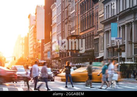 Incrocio trafficato con folle di persone e auto sulla 5th Avenue a Manhattan New York City con luce del tramonto che brilla dietro gli edifici Foto Stock