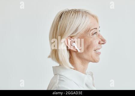 Ritratto laterale di donna matura elegante con cuffie wireless a fuoco, spazio copia Foto Stock