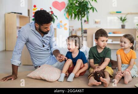 Uomo insegnante che parla con il piccolo ragazzo piangente in aula, confortandolo. Foto Stock