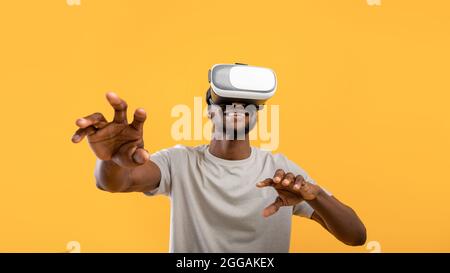 Esperienza virtuale. Felice uomo afroamericano che indossa il visore VR, toccando l'aria mentre gioca al videogioco Foto Stock