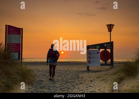 Vista posteriore della giovane donna isolata che cammina sulla spiaggia al tramonto su una spiaggia del Regno Unito, vacanza estiva staycation. Foto Stock