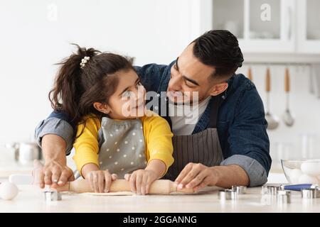 Divertimento al forno. Arab papà e bambina che preparano l'impasto insieme in cucina Foto Stock