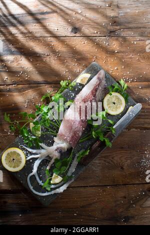 Presentazione di un calamaro fresco e crudo con prezzemolo e limone Foto Stock