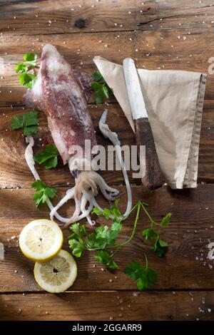 Presentazione di un calamaro fresco e crudo con prezzemolo e limone Foto Stock