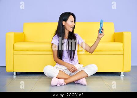Sorridente donna asiatica che fa videochiamata dal telefono delle cellule che parla con gli amici o la famiglia. Tecnologia, concetto di comunicazione Foto Stock