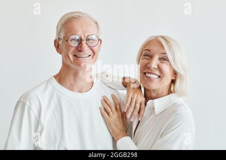 Ritratto minimo di coppia moderna senior indossando bianco su sfondo bianco e sorridendo alla fotocamera Foto Stock