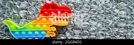 Banner con pop giocattolo è dinosauro arcobaleno colori su uno sfondo bolla. Spazio di copia. Foto Stock