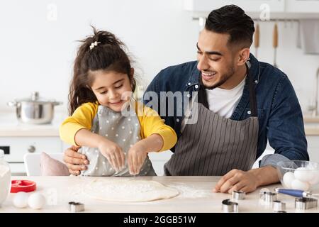 Allegro papà arabo e bambina che cucinano insieme in cucina, facendo la pizza Foto Stock