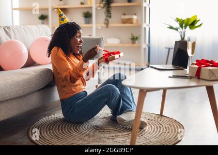 African Lady at laptop Opening Gift Celebring Birthday Online Indoor Foto Stock