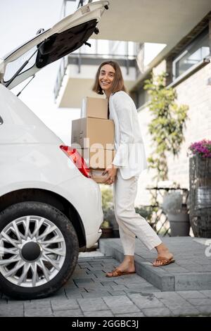 Donna con un pacchi vicino alla sua auto e a casa Foto Stock