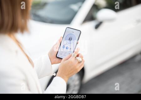 La donna chiude la porta o accende la sveglia con un telefono cellulare. Dispositivo con programma in esecuzione per la sicurezza del veicolo. Tecnologie innovative in auto Foto Stock
