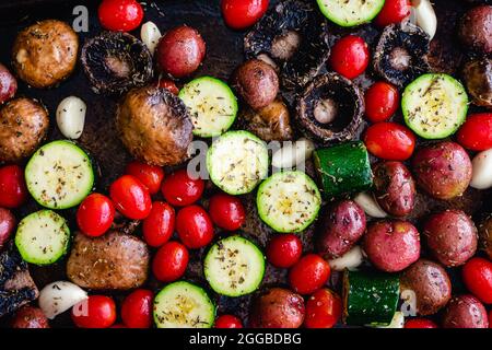 Verdure italiane non cotte in olio d'oliva e spezie: Pomodori crudi, zucchine, funghi, patate rosse, spicchi d'aglio su un tegame Foto Stock