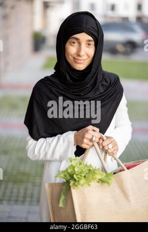 Donna musulmana con generi alimentari vicino alla casa Foto Stock