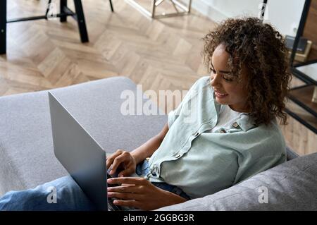 Giovane afro americano donna blogger seduto sul divano a casa digitando sul portatile. Foto Stock