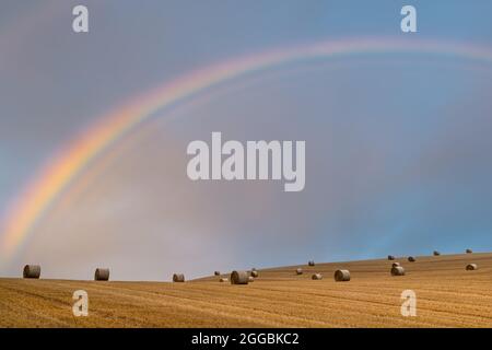 Balle di fieno pronte per la raccolta come un arcobaleno appare nel cielo Foto Stock