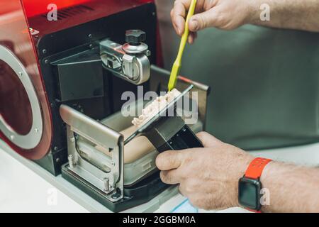 Mano dell'uomo che raccoglie l'eccesso di resina da una stampante dentale 3D in un laboratorio dentale Foto Stock