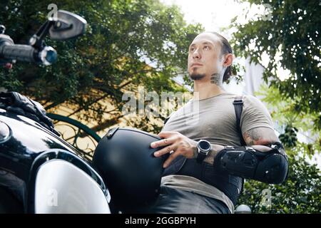 Giovane uomo serio con casco seduto in moto e togliere il casco Foto Stock