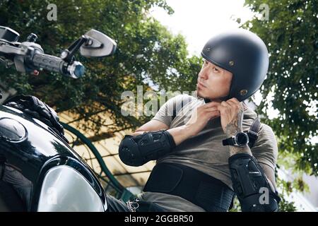 Un giovane uomo serio che guarda lo specchio del motociclo quando si indossa il casco per proteggersi Foto Stock