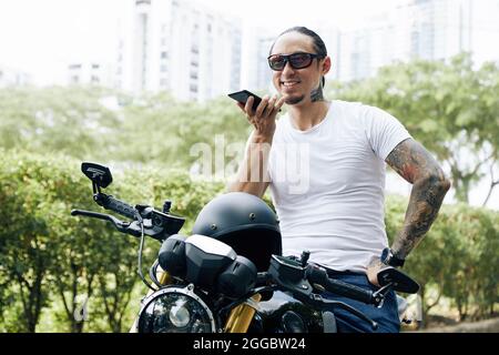 Happy FIT uomo seduto sul motocicletto e registrare messaggio vocale per amico Foto Stock