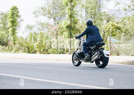 Uomo in jeans e giacca denim a cavallo in moto su autostrada, vista dal retro Foto Stock