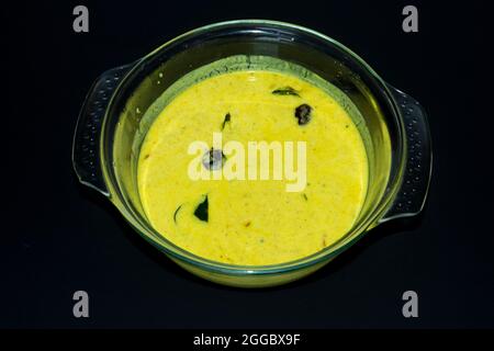 Primo piano immagine di Kerala Onam Speciale tradizionale Curry giallo Buttermilk noto anche come Moru Curry, Pulissery, Kachiya Moru in Glass Bowl. Nero Backgr Foto Stock