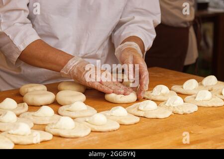 La donna nella foto sta facendo torte ripiene. Guanti protettivi avvolge il ricciolo nella pasta di lievito. Lavoro nel panificio. Foto Stock