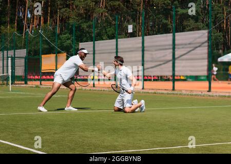 Eccitati giocatori di tennis multietnici che scuotono le mani sul campo Foto Stock