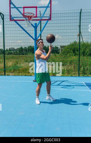 Giovane sportivo che gira la palla di basket a un dito sul parco giochi Foto Stock