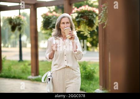 Donna con borsetta che beve caffè nel parco Foto Stock
