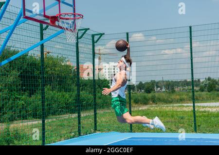 Vista laterale dello sportivo che salta sotto l'anello mentre gioca a streetball Foto Stock