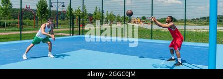 Vista laterale di sportivi interrazziali che giocano a streetball, banner Foto Stock