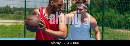 Uomo afroamericano che gioca a streetball con amici all'aperto, banner Foto Stock