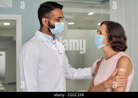 Cheerful medico indiano che sostiene la paziente più anziana femminile in maschere in ospedale. Foto Stock