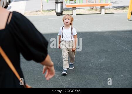 Piangendo il ragazzo di quattro anni che cammina sull'asfalto alla madre per abbracci e conforto. Da dietro la donna, spalla. Foto Stock