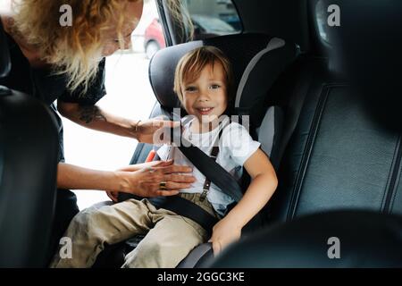 Mamma che aiuta suo figlio piccolo a regolare la cintura di sicurezza in un'auto. Dall'interno di un salone. Foto Stock